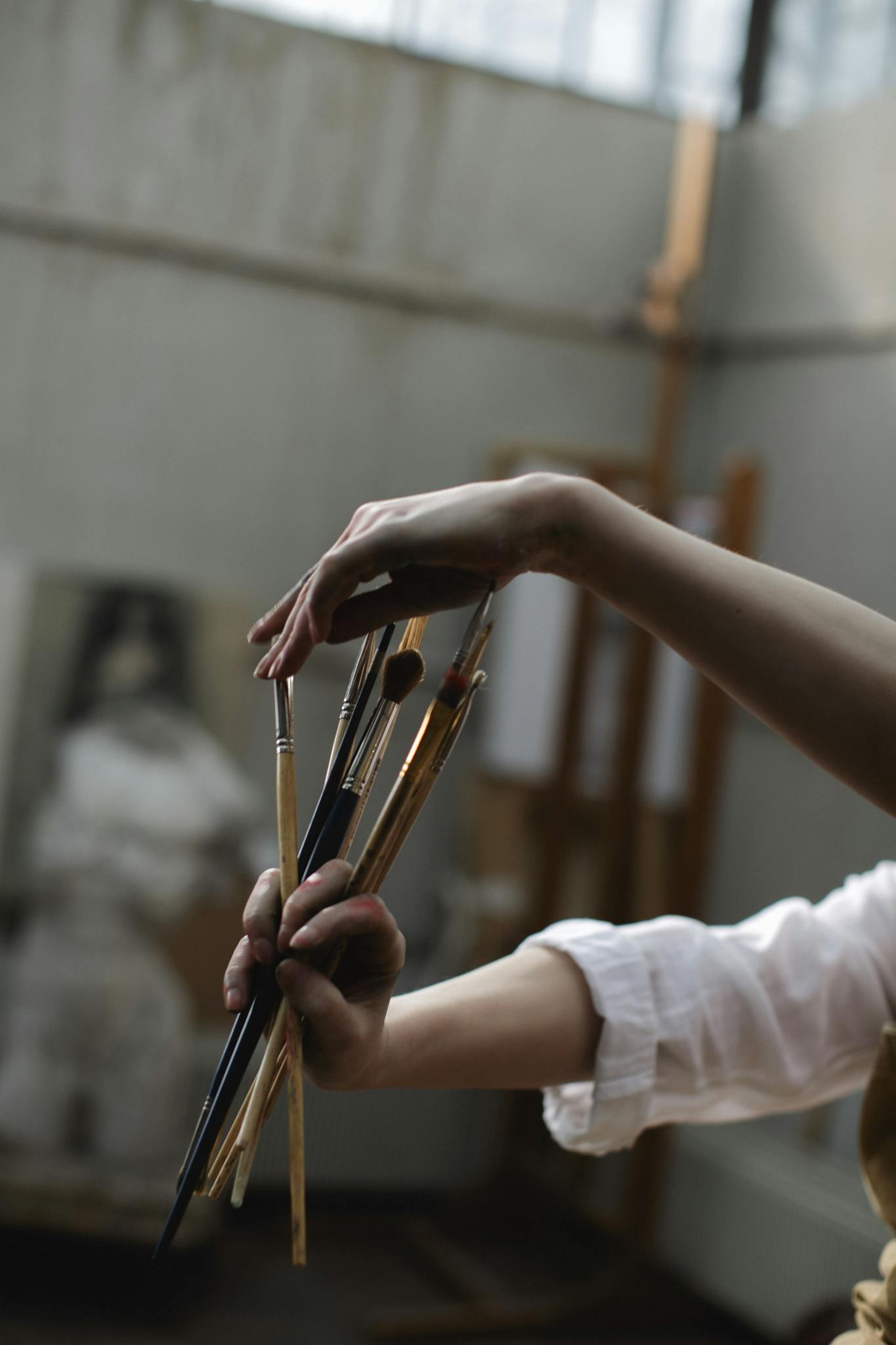 Close-up of an artist's hands holding paintbrushes indoors, showcasing creativity and artistry.
